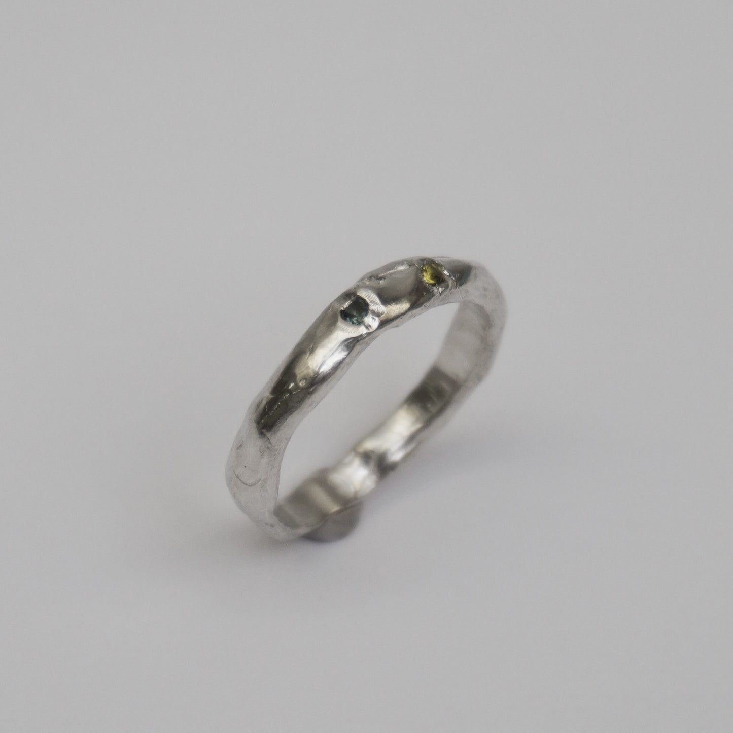 Artisanal handmade silver ring with organic, slim band and two embedded synthetic stones in green and blue tones. Unique one-of-a-kind jewelry piece crafted from solid 925 sterling silver using lost-wax casting. Sculptural, slightly irregular finish with minimal, contemporary design. Created in a small studio in Porto.