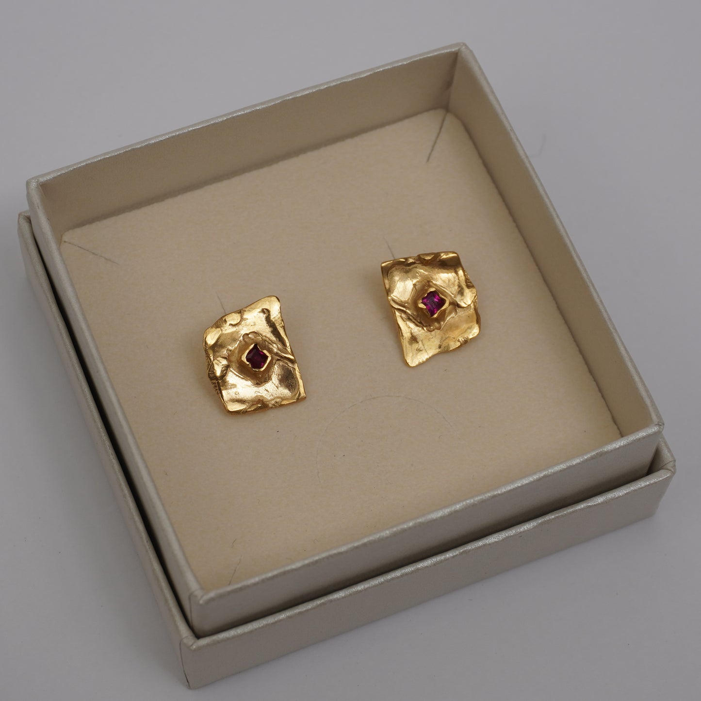 Gold-plated handcrafted stud earrings with organic sculptural surfaces and red hand-set gemstones