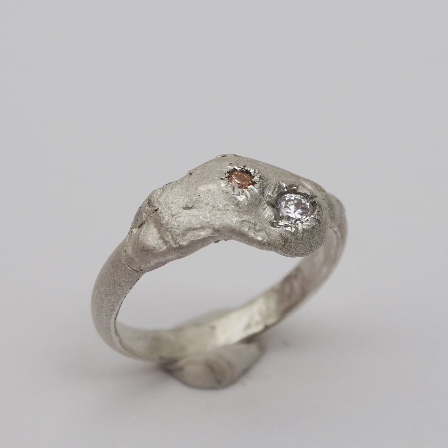 Handcrafted artisanal silver ring with a sculptural, raw-textured band and two asymmetrically embedded zirconia stones in champagne and clear tones. Unique, organic design made using the lost-wax casting technique. Contemporary handmade jewelry with an expressive, irregular surface and elevated artistic detail.