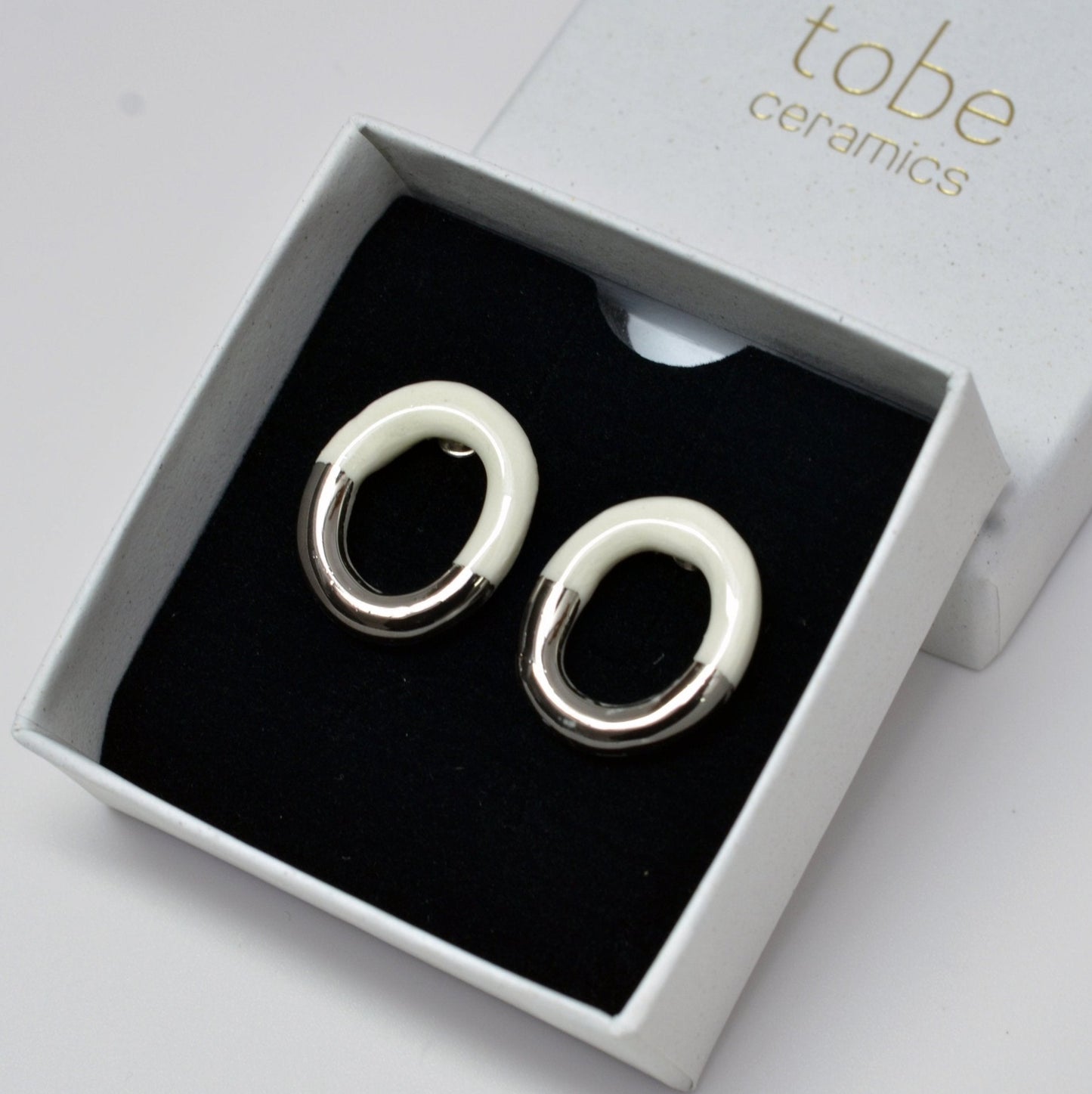 Artisanal Handmade Porcelain Earrings With a Modern Two-Tone Design – Half Natural White Ceramic, Half Glazed in Either Gold or Silver. Lightweight Oval-Shaped Hoops That Blend Minimalist Elegance With a Bold, Contemporary Look. Perfect for Statement Jewelry Lovers Seeking Unique, Handcrafted Pieces.
