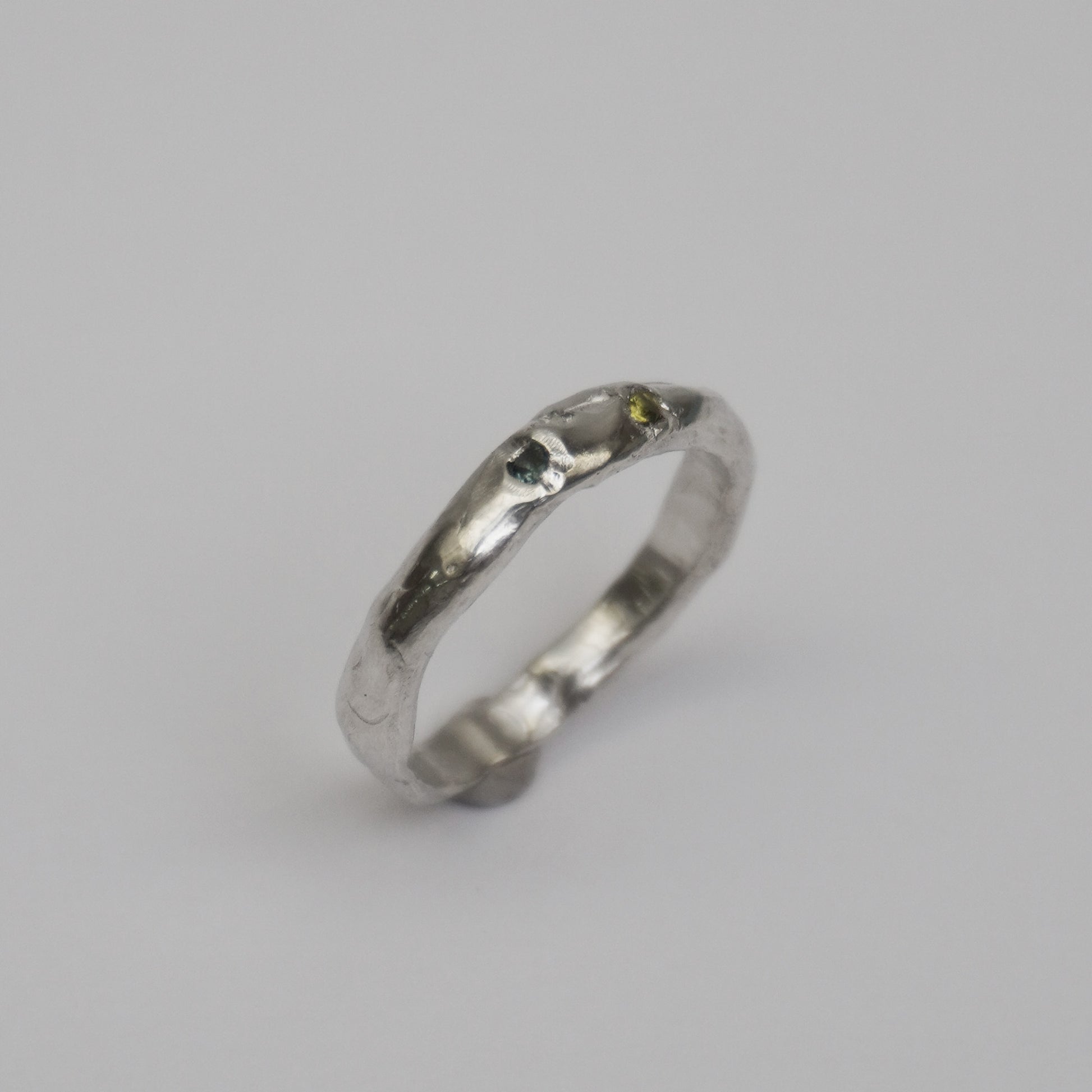 Artisanal handmade silver ring with organic, slim band and two embedded synthetic stones in green and blue tones. Unique one-of-a-kind jewelry piece crafted from solid 925 sterling silver using lost-wax casting. Sculptural, slightly irregular finish with minimal, contemporary design. Created in a small studio in Porto.


