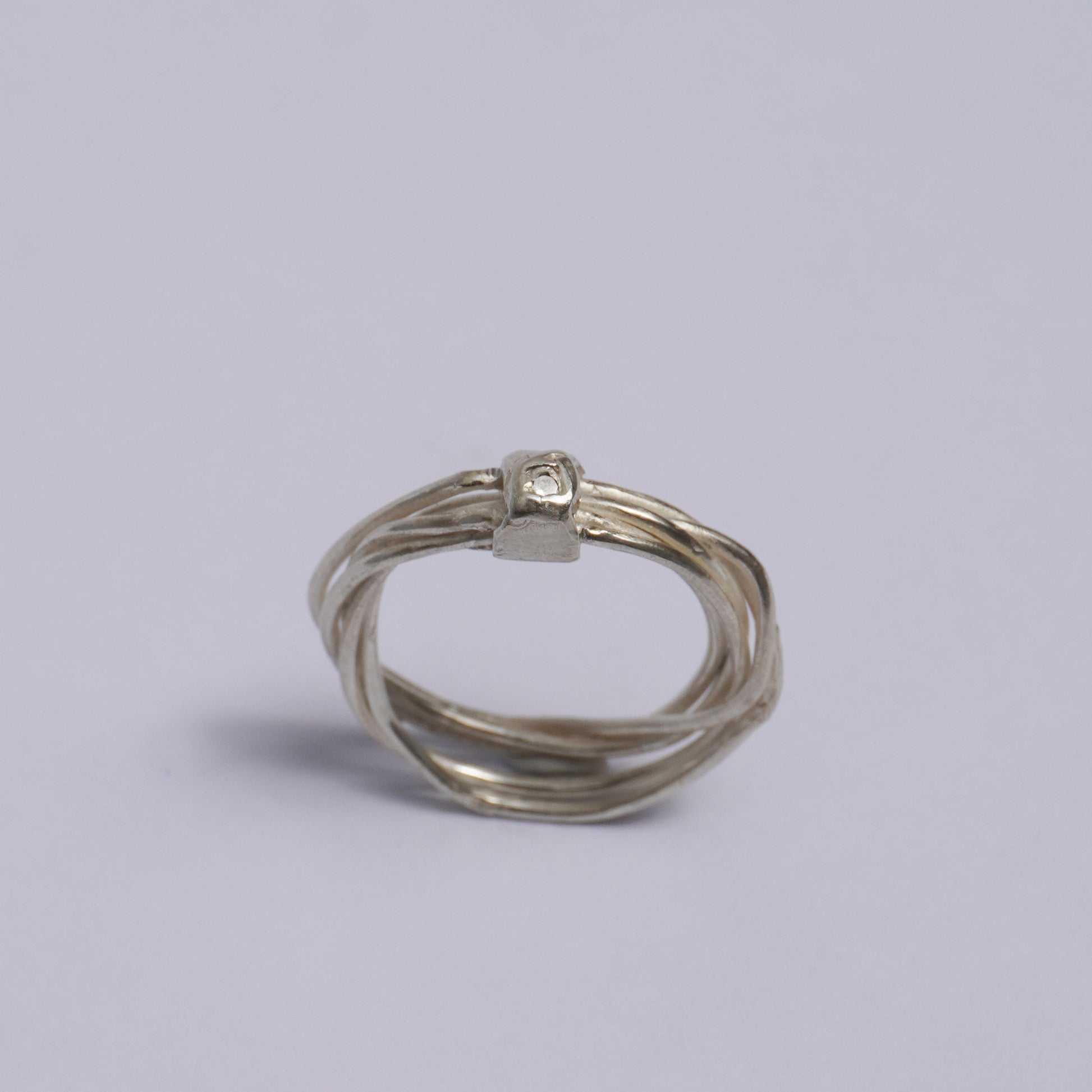 Handmade artisanal silver ring featuring multiple interwoven bands fused into a single unique form, accented by a small raised detail with an embedded clear zirconia stone. Crafted using the lost-wax casting technique in a Porto-based studio, this one-of-a-kind piece embodies slow design and sculptural elegance.