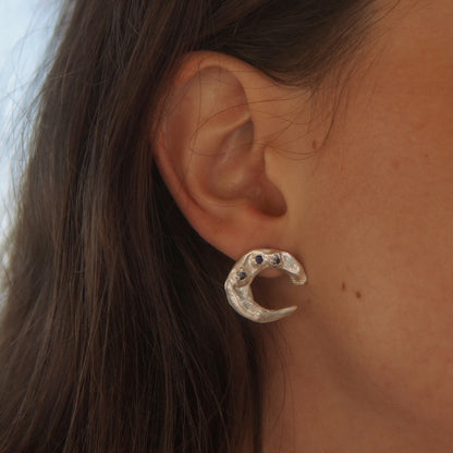 Close-up of an ear wearing a silver moon earring with dark gemstones