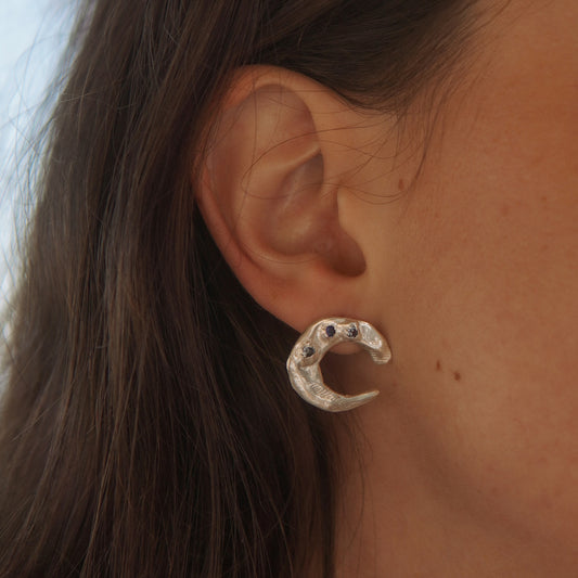 Close-up of an ear wearing a silver moon earring with dark gemstones