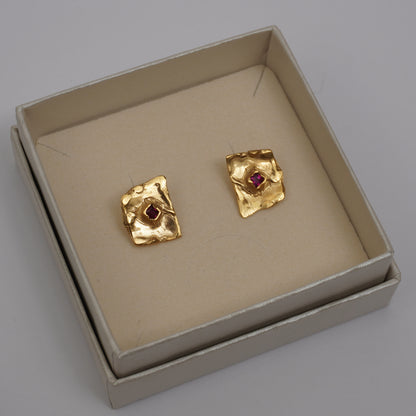 Gold-plated handcrafted stud earrings with organic sculptural surfaces and red hand-set gemstones