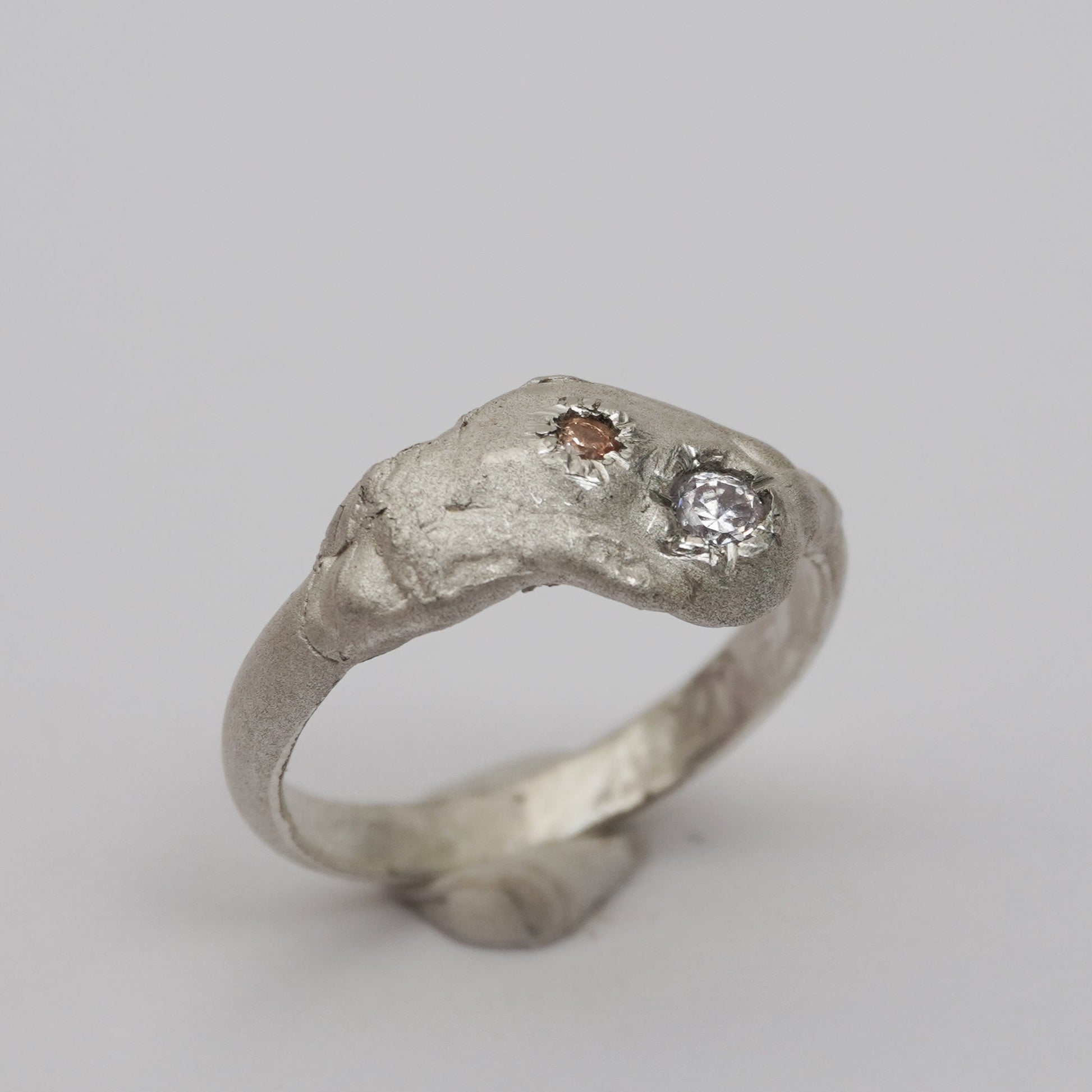 Handcrafted artisanal silver ring with a sculptural, raw-textured band and two asymmetrically embedded zirconia stones in champagne and clear tones. Unique, organic design made using the lost-wax casting technique. Contemporary handmade jewelry with an expressive, irregular surface and elevated artistic detail.