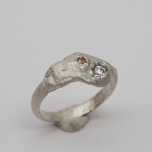 Handcrafted artisanal silver ring with a sculptural, raw-textured band and two asymmetrically embedded zirconia stones in champagne and clear tones. Unique, organic design made using the lost-wax casting technique. Contemporary handmade jewelry with an expressive, irregular surface and elevated artistic detail.