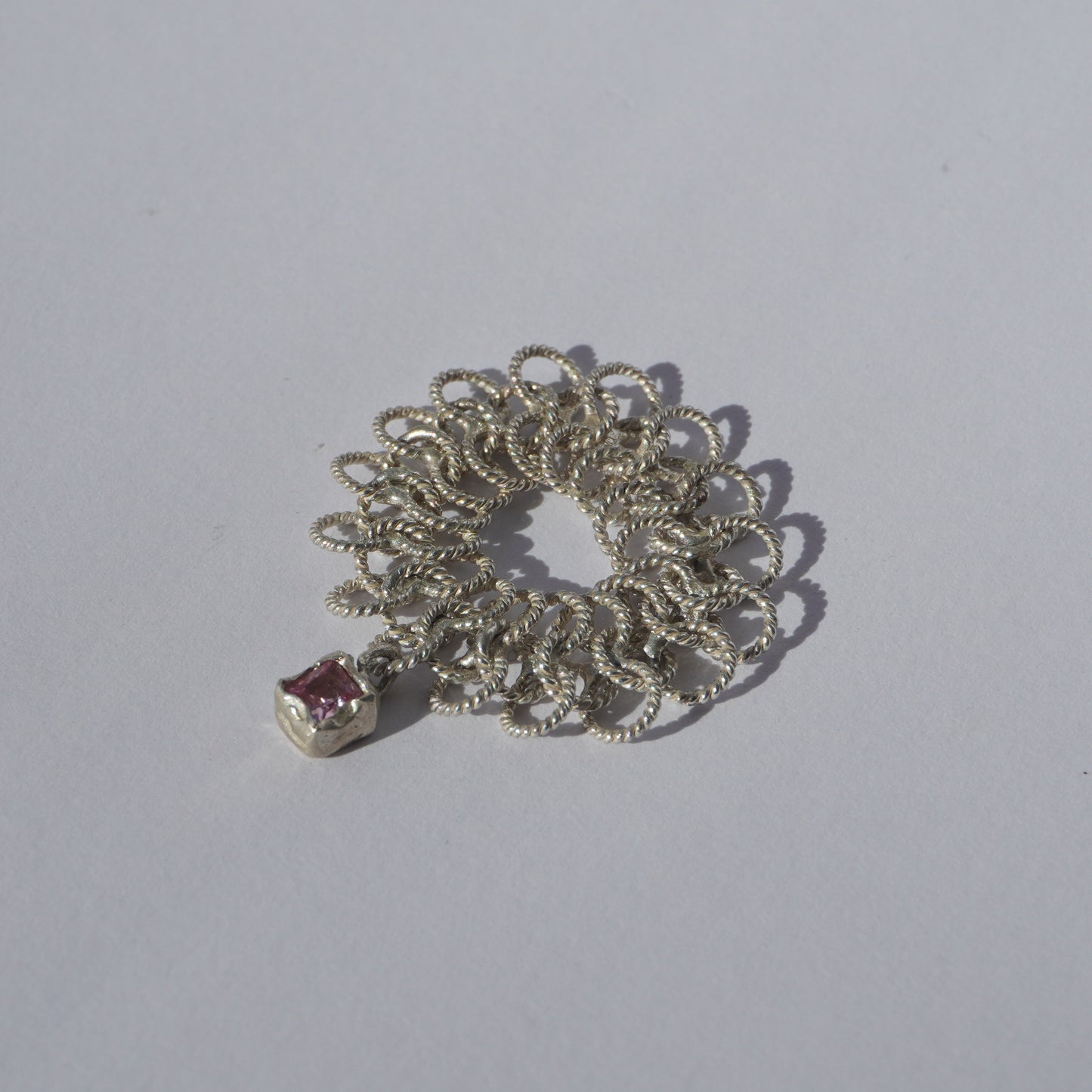 Handcrafted silver ring made of twisted interlinked loops with a hanging pink square-cut gemstone