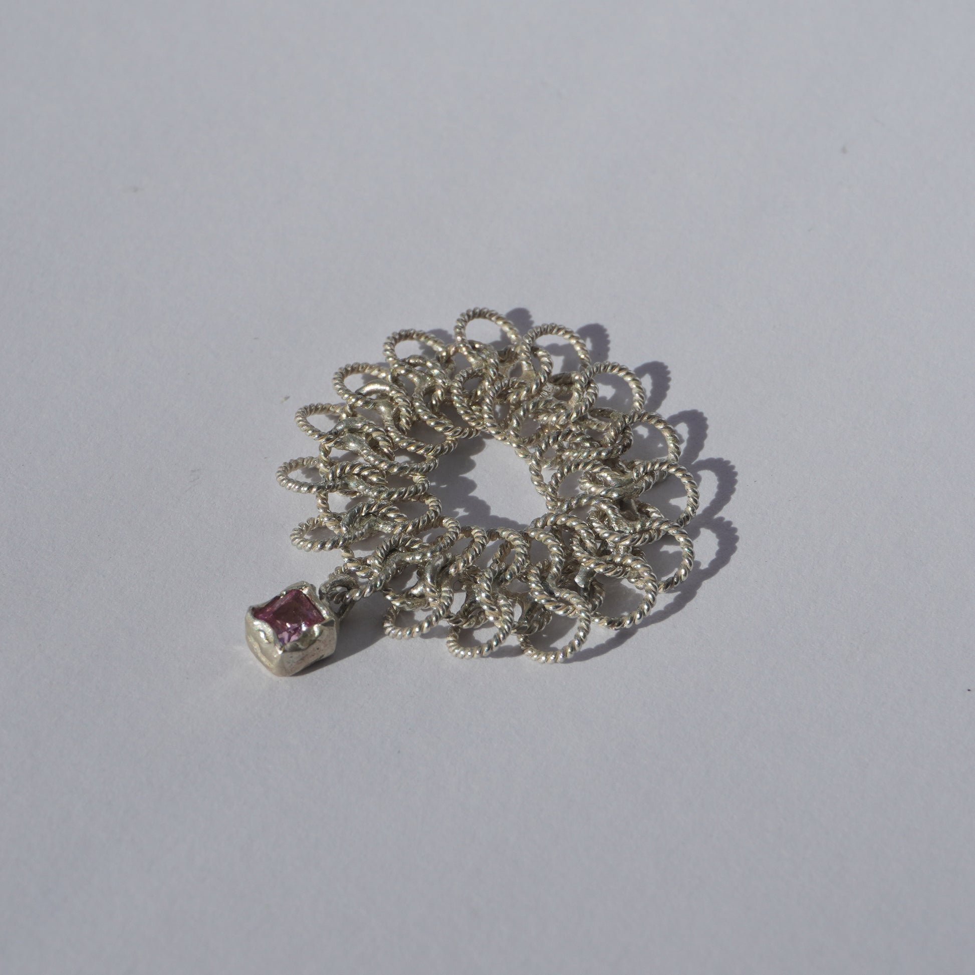 Handcrafted silver ring made of twisted interlinked loops with a hanging pink square-cut gemstone