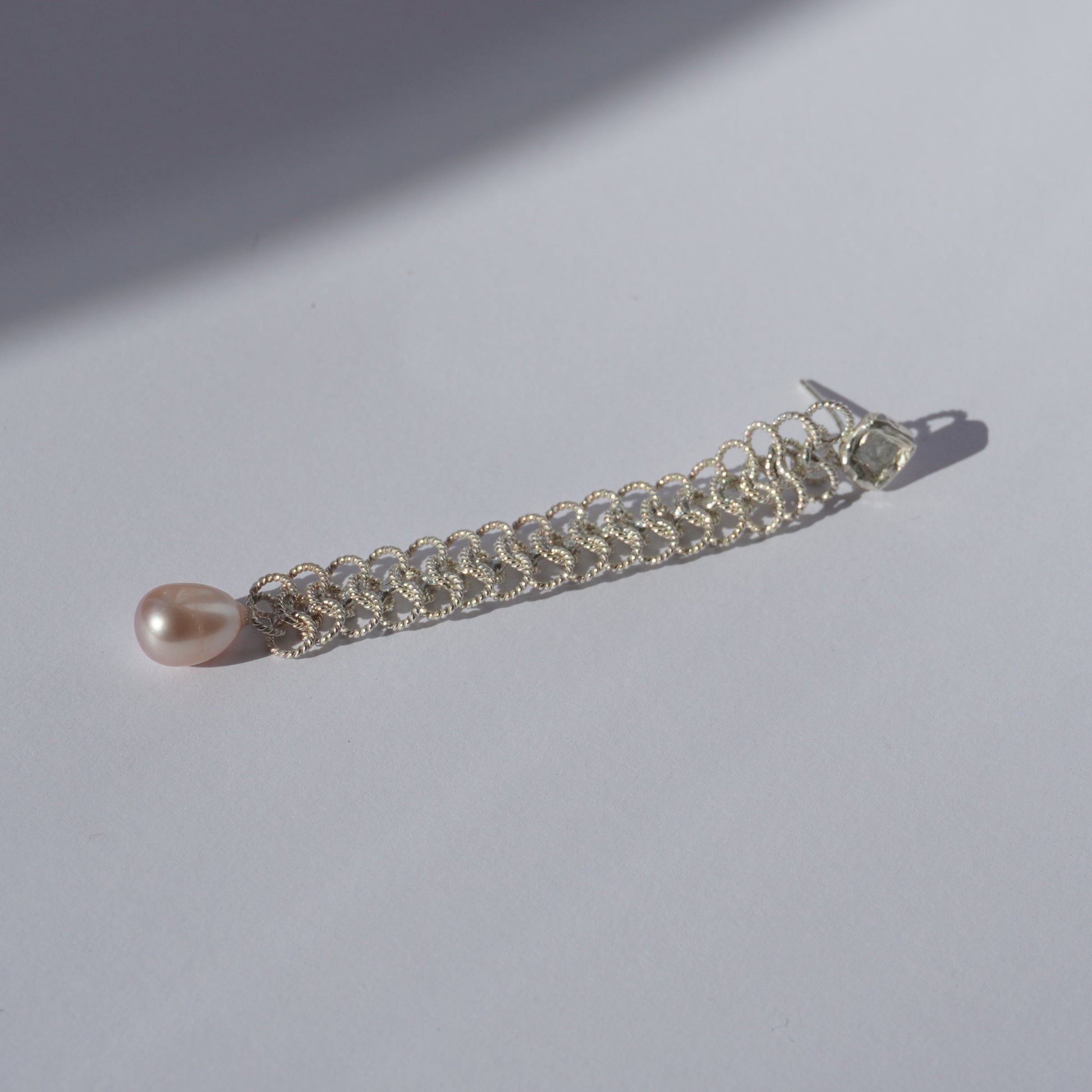 Handcrafted silver earring with lace-like chain, freshwater pearl, and hand-set gemstone