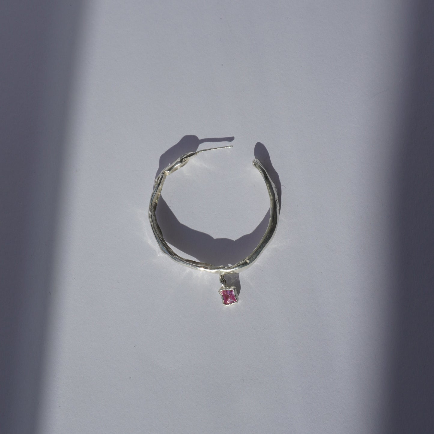 Handcrafted silver hoop earring with irregular organic shape and pink hand-set gemstone