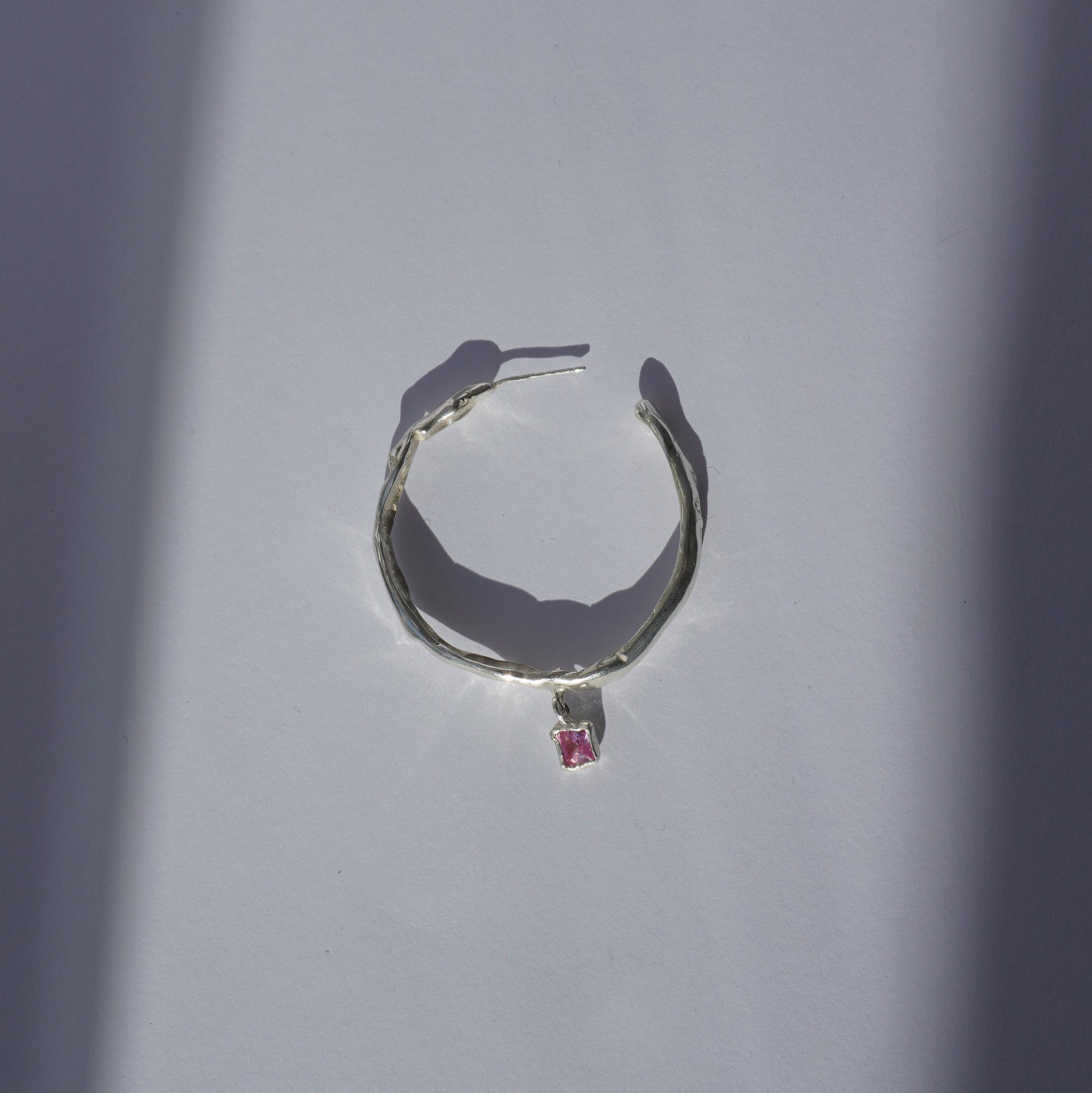 Handcrafted silver hoop earring with irregular organic shape and pink hand-set gemstone