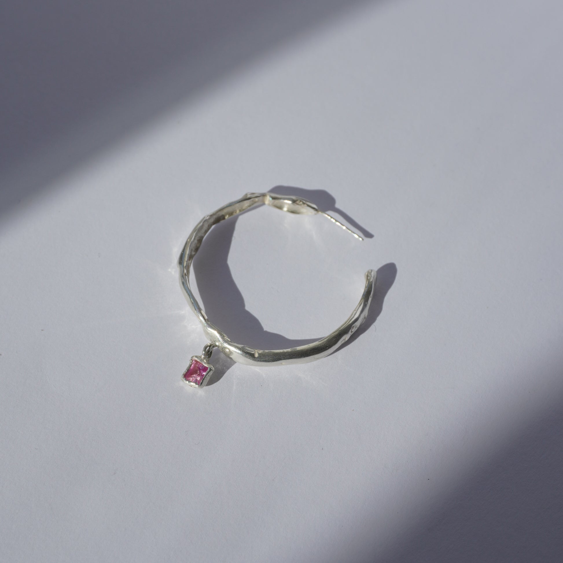 Handcrafted silver hoop earring with irregular organic shape and pink hand-set gemstone