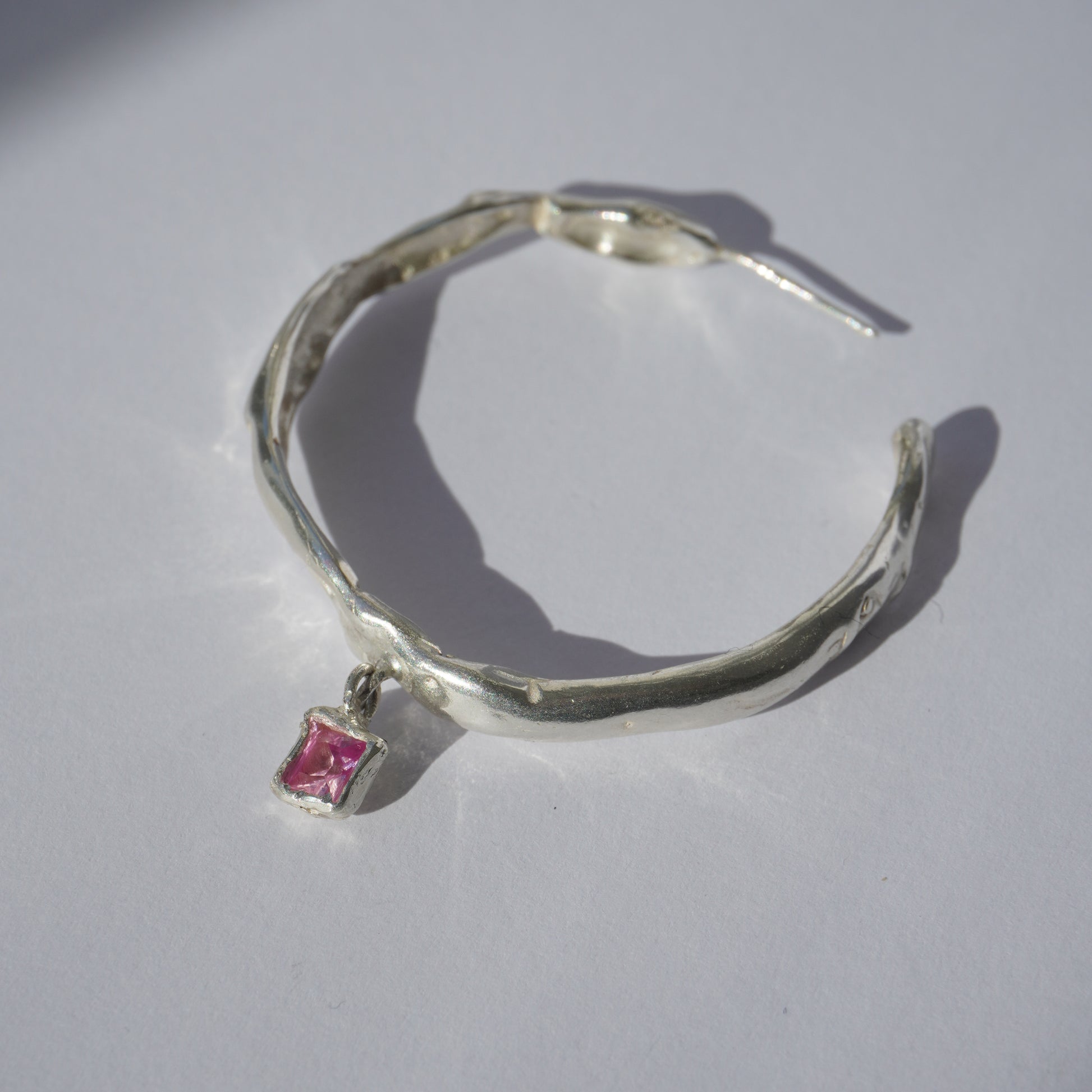 Handcrafted silver hoop earring with irregular organic shape and pink hand-set gemstone