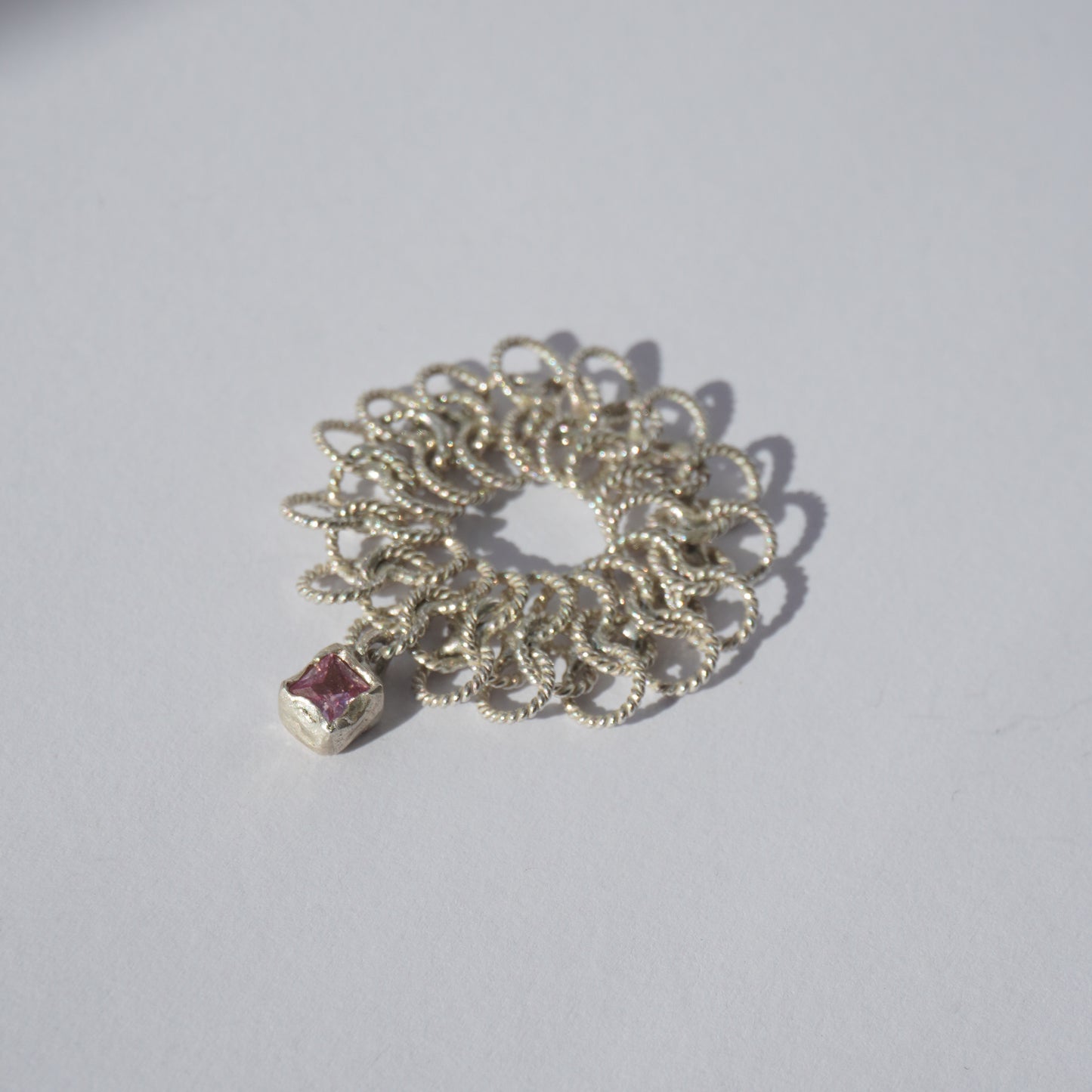 Handcrafted silver ring made of twisted interlinked loops with a hanging pink square-cut gemstone