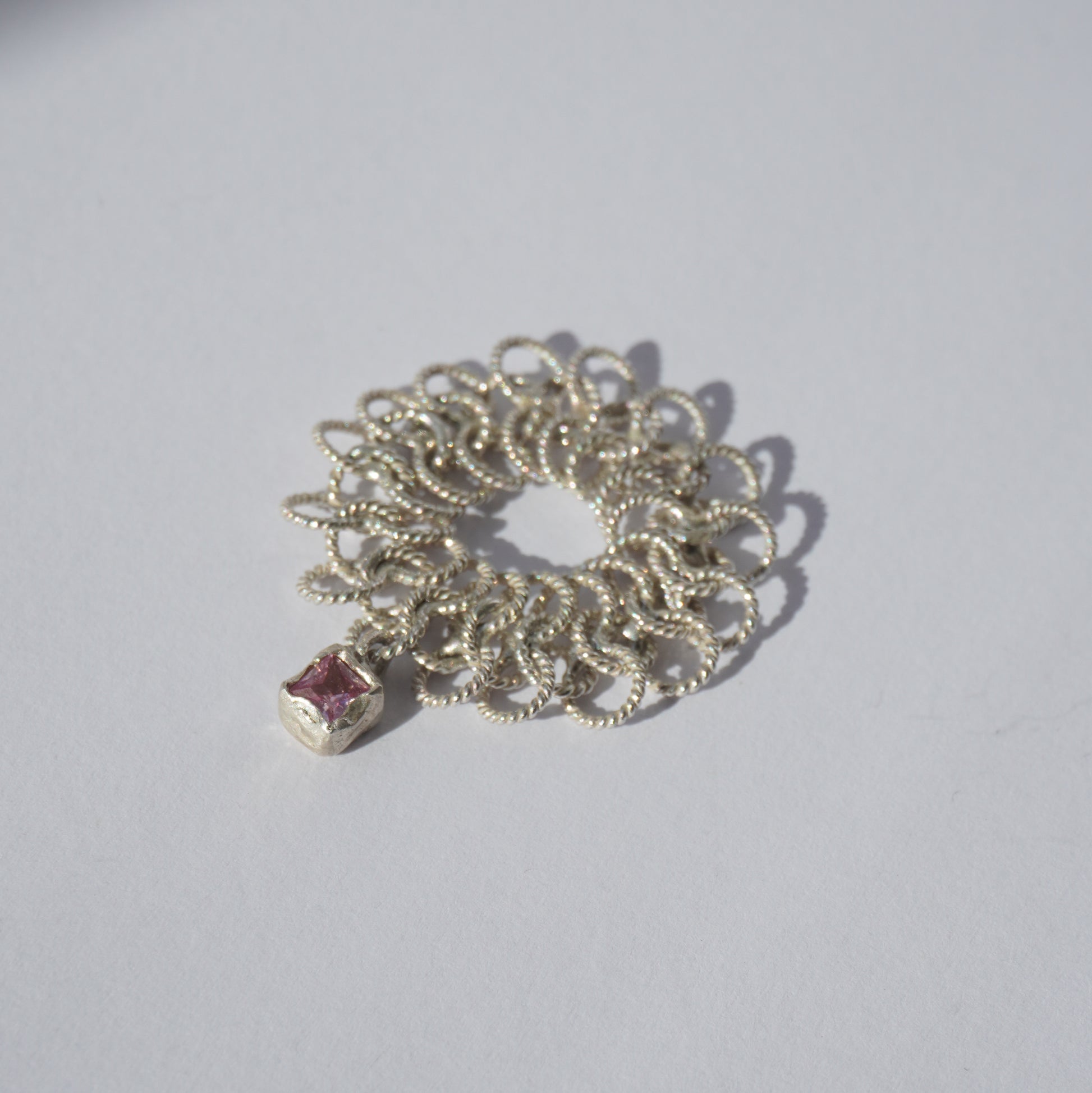 Handcrafted silver ring made of twisted interlinked loops with a hanging pink square-cut gemstone