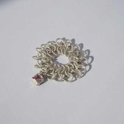 Handcrafted silver ring made of twisted interlinked loops with a hanging pink square-cut gemstone
